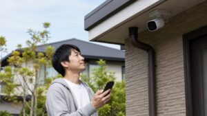 戸建て屋外に設置した防犯カメラをスマホで確認する日本人男性