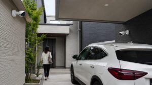 住宅の駐車場とカーポートに設置された複数の防犯カメラで車周辺を監視する様子