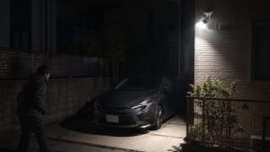 夜の駐車場でセンサーライト付き防犯カメラが車と不審者の接近を照らす様子