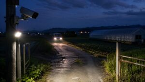 夜間の農道入口を監視する防犯カメラとセンサーライトの設置例