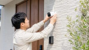 日本の住宅玄関で男性が電源不要のワイヤレス防犯カメラを外壁に設置している様子